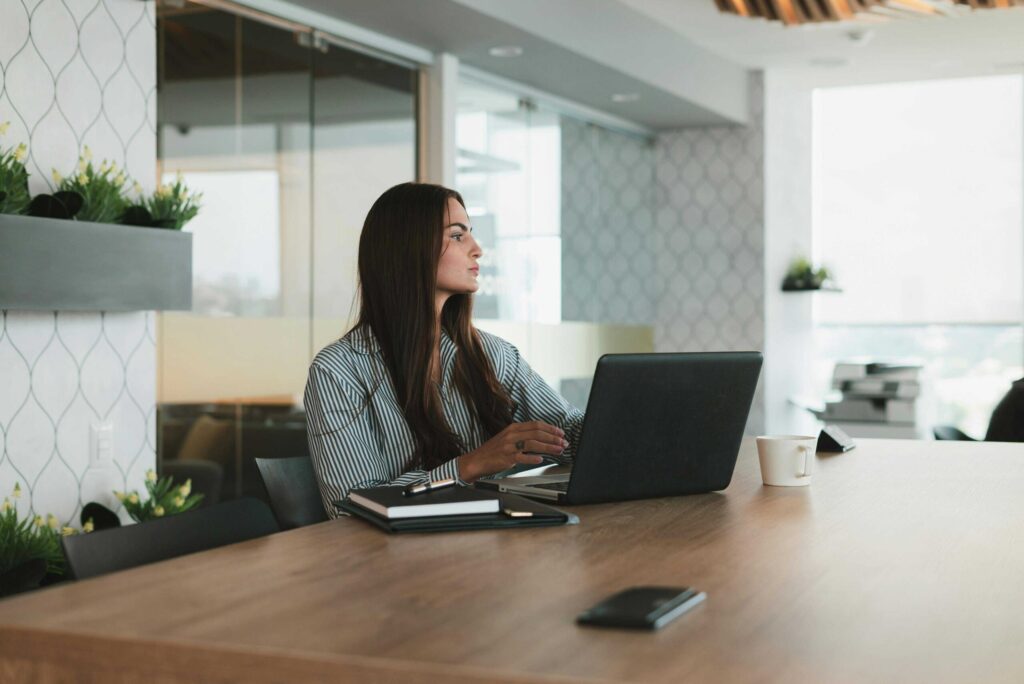 Professional woman working at a laptop in a modern office, with plants on the side and a coffee mug on the desk