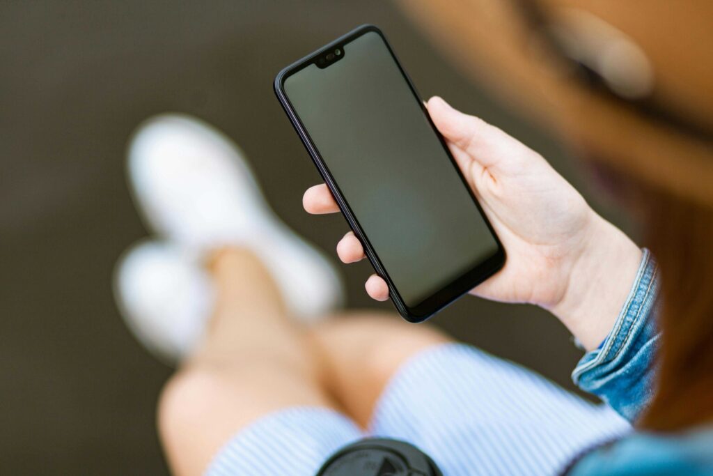 Person holding a black smartphone with a blank screen, visible denim sleeve.