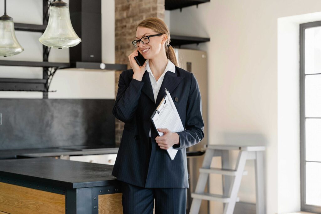Professional woman in a navy pinstripe suit and glasses, on a call beside a kitchen island in a modern space.