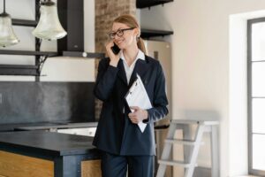 Professional woman in a navy pinstripe suit and glasses, on a call beside a kitchen island in a modern space.