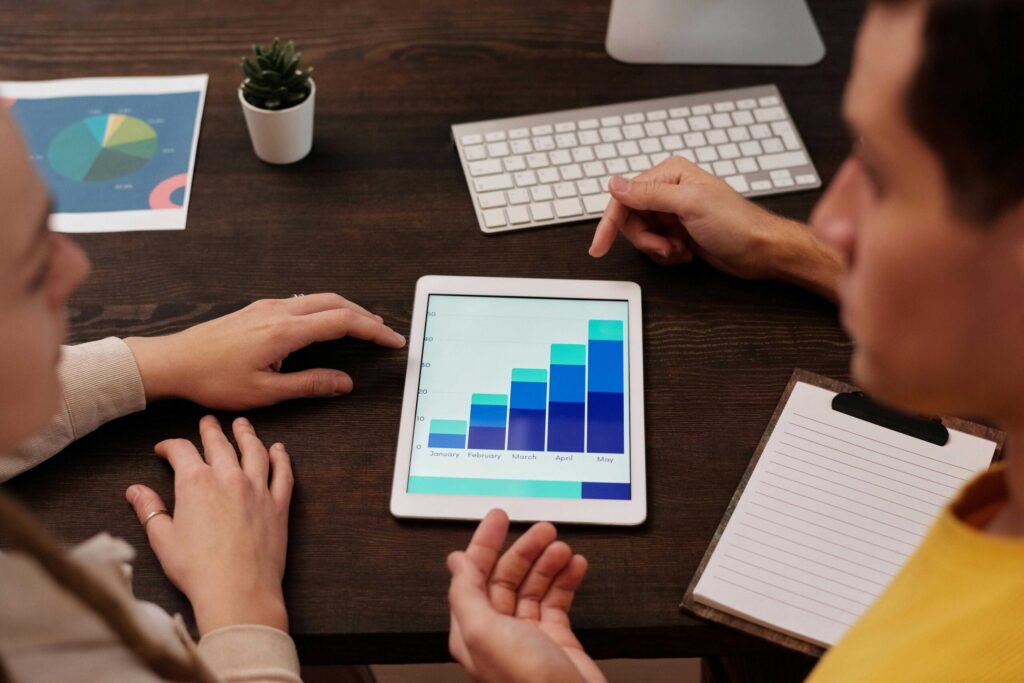 Group of people around a desk examining a tablet displaying a stacked bar chart (months labeled January to May).