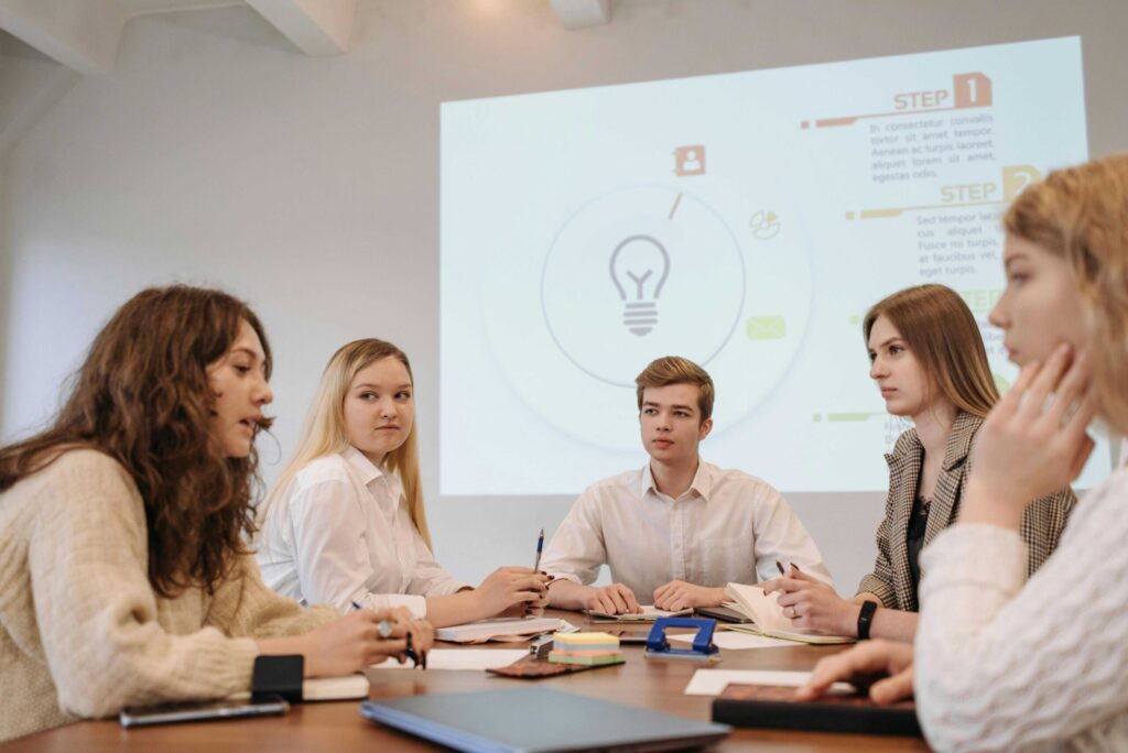 Group of young adults in a meeting around a table with a projected presentation behind them