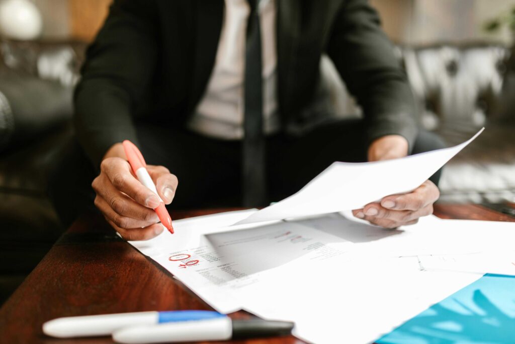Close-up of a person in a dark suit signing and marking documents with an orange marker at a wooden table