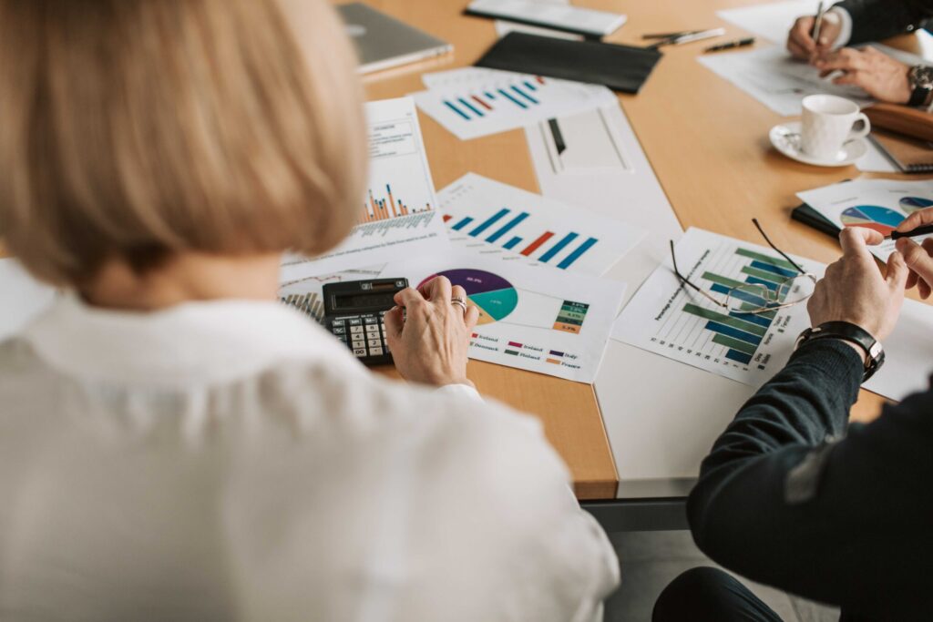 Team discussing financial charts spread across a wooden table, with a calculator and coffee cup nearby.