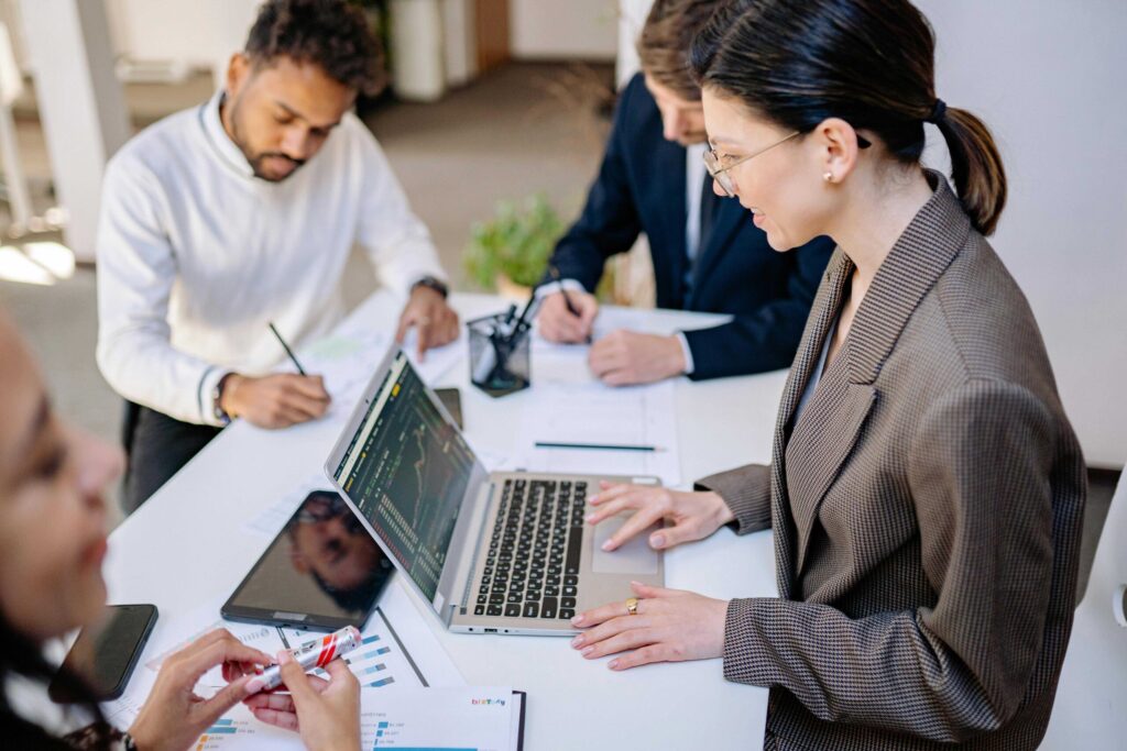 Team of professionals in a meeting with laptops open, reviewing charts on a white table in a bright office context
