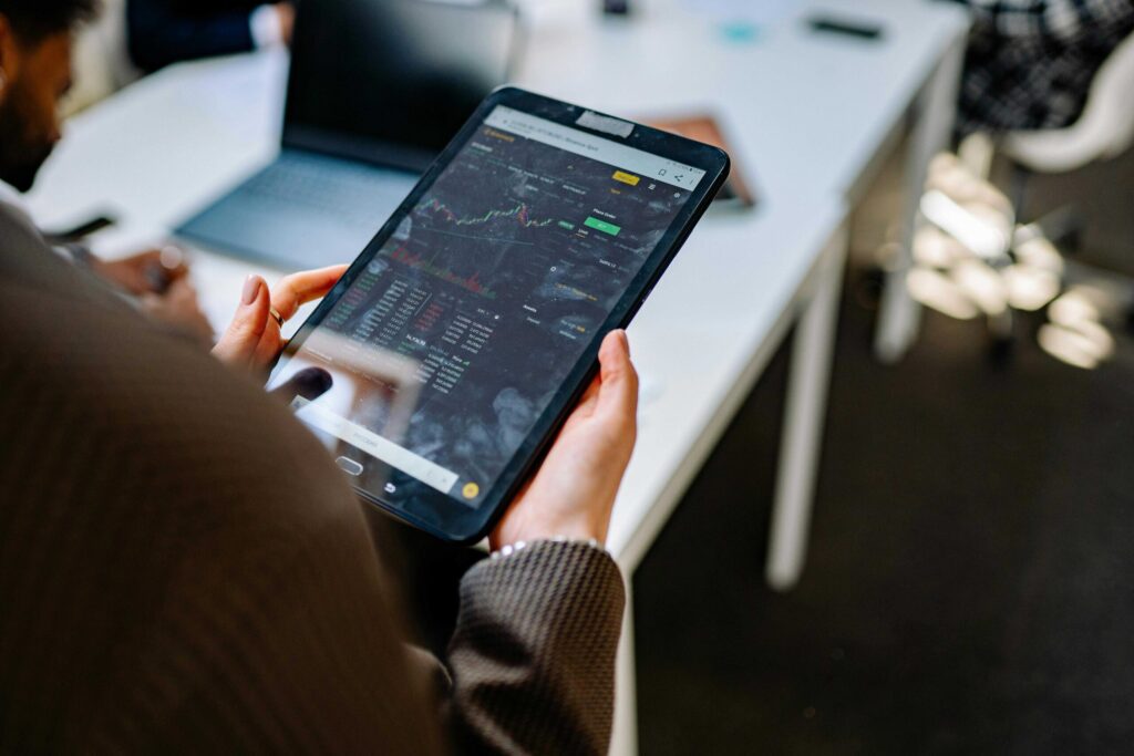 Close-up of hands holding a tablet displaying stock market charts and trading data.