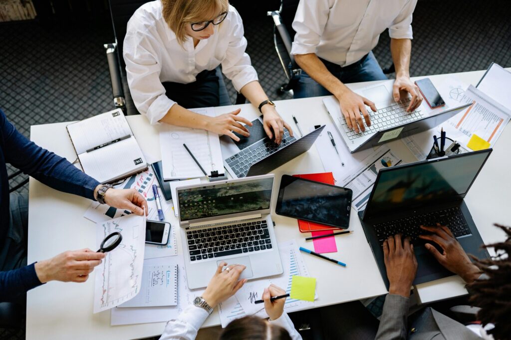Overhead view of a collaborative work session with several laptops, papers, and sticky notes on a white table.