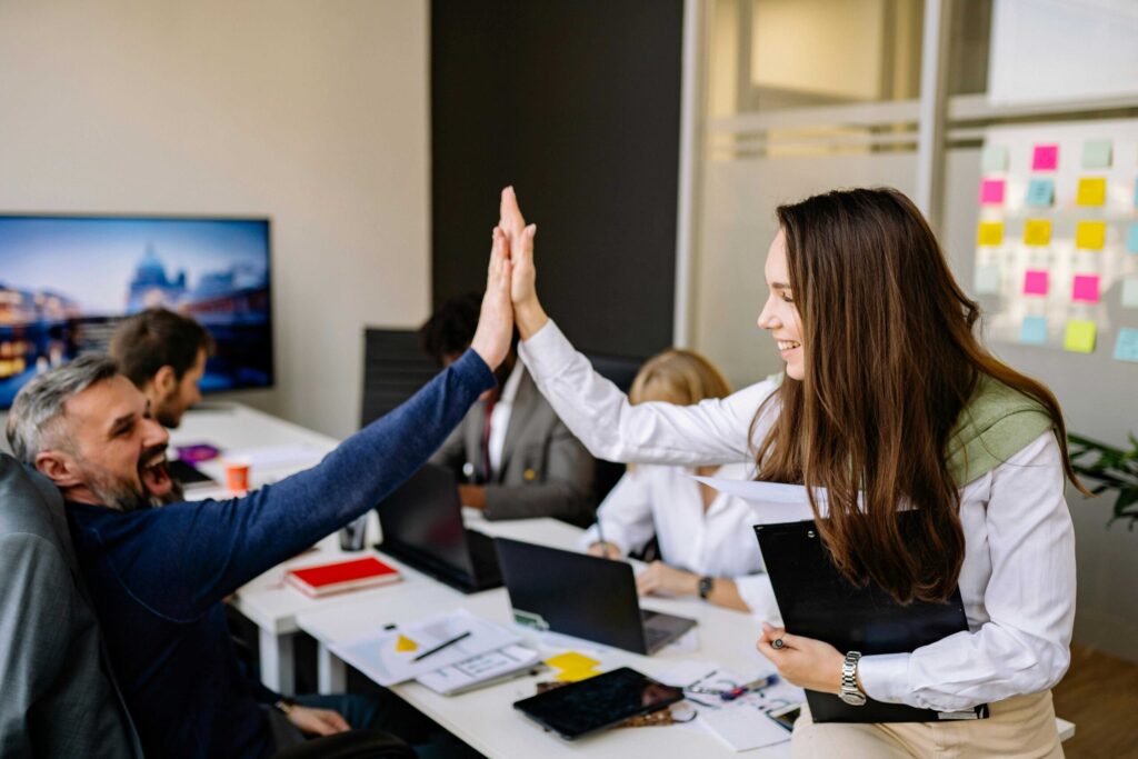 Team members in a bright office high-fiving to celebrate a win or agreement.