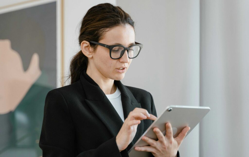 Woman in a black blazer using a tablet, looking at the screen in a professional setting.