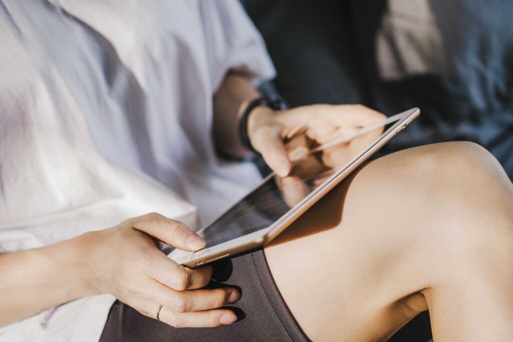 Close-up of hands holding a tablet and using a stylus on the screen, on a person’s lap